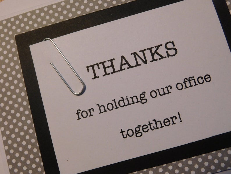 May include: A white card with black text and a silver paperclip. The text reads "THANKS for holding our office together!"