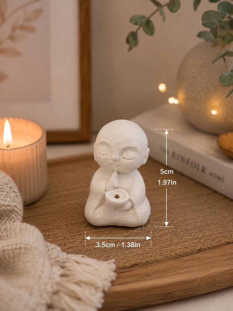 May include: A small white matte figurine of a seated person with closed eyes, holding a circular bowl. The figure measures 1.97 inches in height and 1.38 inches in width. The surface has a textured finish, and the figure is depicted in a meditative pose.