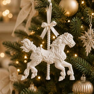 May include: A white carousel horse ornament featuring intricate floral and saddle detailing, suspended by a matching white satin ribbon tied in a bow at the top of a twisted pole. The horse is depicted in a galloping pose with a flowing mane and tail.