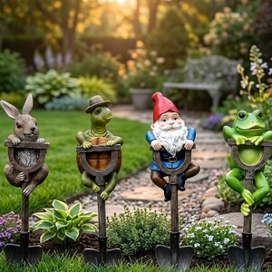 Peut inclure: Quatre tuteurs de jardin représentant des figurines sculptées : un lapin brun, une tortue verte avec un chapeau, un gnome au bonnet rouge et à la barbe blanche, et une grenouille verte. Chaque figurine est fixée sur un piquet en forme de pelle.