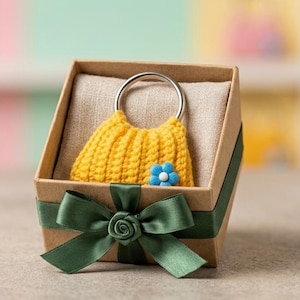 May include: A yellow crocheted handbag with a silver ring handle and a blue flower accent, presented in a brown gift box with a green satin bow. The box is lined with beige fabric.