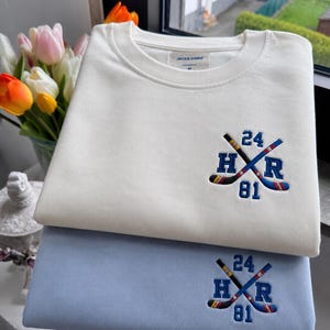 Può includere: Una felpa color crema e una felpa azzurra, entrambe caratterizzate da un ricamo raffigurante due mazze da hockey incrociate, le lettere H e R e i numeri 24 e 81. La felpa color crema presenta un'etichetta del marchio Jack & Jones.