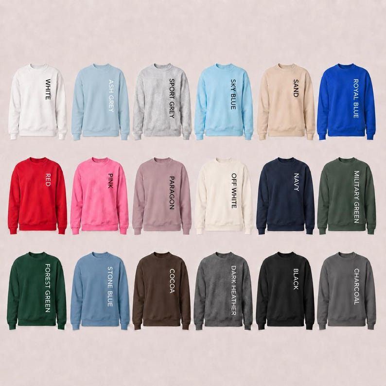 May include: A collection of eighteen crewneck sweatshirts displayed in a grid, each featuring a different solid color including white, ash grey, sport grey, sky blue, sand, royal blue, red, pink, paragon, off white, navy, military green, forest green, stone blue, cocoa, dark heather, black, and charcoal, with the color name printed vertically in black text on the right side of each garment.