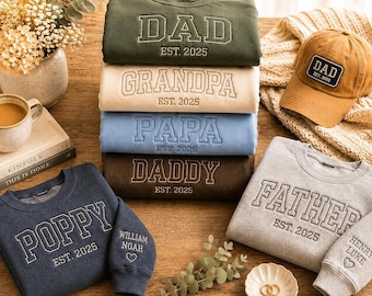May include: A collection of crewneck sweatshirts and a baseball cap featuring embroidered text. The sweatshirts are in olive, beige, light blue, dark brown, navy, and gray, with text including DAD, GRANDPA, PAPA, DADDY, POPPY, and FATHER, all with EST. 2025.