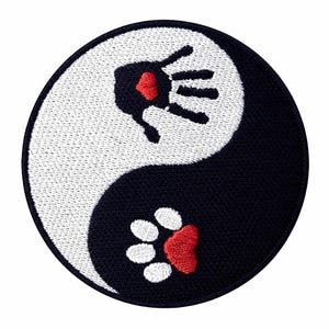Puede incluir: Un parche redondo bordado con un diseño de Yin y Yang. La mitad blanca tiene una huella de mano negra con un corazón rojo, y la mitad negra tiene una huella de pata blanca con un corazón rojo.