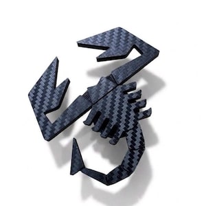 May include: A scorpion-shaped emblem featuring a dark gray and black carbon fiber weave pattern. The object displays a stylized, angular design with distinct segments forming the claws, body, and a curved tail, all rendered in a textured finish.
