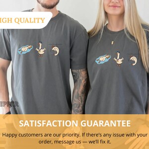 May include: Two gray t-shirts with a cartoon goose design. The design shows a goose in a pool, a goose with a medal, and a goose diving. The text "HIGH QUALITY" is at the top. The text "SATISFACTION GUARANTEE" is at the bottom.