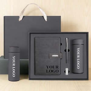 Könnte beinhalten: Ein dunkelgraues Geschenkset mit Notizbuch, Stift, Becher und Geschenktüte. Das Notizbuch hat einen Verschluss und den Text "YOUR LOGO". Der Becher und das Notizbuch tragen den Text "YOUR LOGO" in Weiß. Das Set wird in einer dunkelgrauen Box präsentiert.
