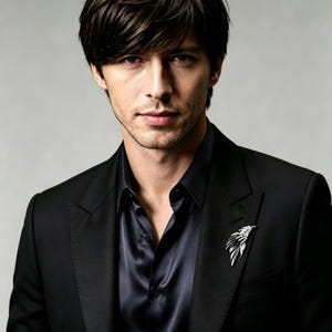 Pode incluir: Casaco preto com camisa de cetim azul escuro. Um broche prateado em forma de asa é preso na lapela esquerda. A pessoa na imagem tem cabelo escuro e uma expressão neutra.