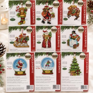 May include: A collection of nine Dimensions counted cross stitch ornament kits in individual plastic packaging. The designs feature festive themes including a teddy bear in a stocking, Santa Claus, a reindeer, a sleigh, a snowman, and Christmas trees.