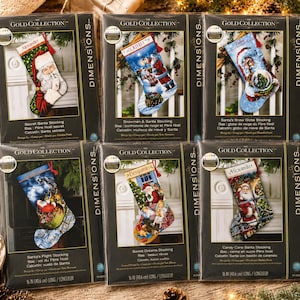 Op de afbeelding: Zes Dimensions Gold Collection kruissteek kerstsokpakketten in individuele plastic verpakking. Elk pakket bevat een uniek kerstontwerp met de Kerstman, sneeuwpoppen en winterscènes met labels zoals Secret Santa en Candy Cane Santa Stocking.