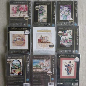 Puede incluir: Una colección de kits de punto de cruz Dimensions Gold Collection Petites. Los kits presentan diseños florales, una tetera, una taza de té y una geisha. Cada kit está empaquetado en una funda de plástico transparente con un borde negro y dorado.