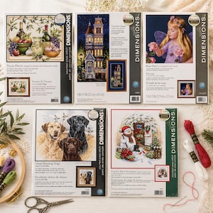 May include: A selection of Dimensions counted cross-stitch kits. The kits showcase diverse designs, such as a Tuscan still life, a Victorian house, a fairy, a group of dogs, and a snowman scene. Each kit contains all the materials needed.