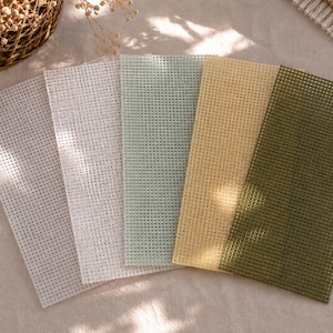 May include: A set of five rectangular plastic canvas sheets arranged in a fan shape. The colors include light gray, white, pale mint green, soft yellow, and olive green. Each sheet features a uniform grid pattern of small square holes.