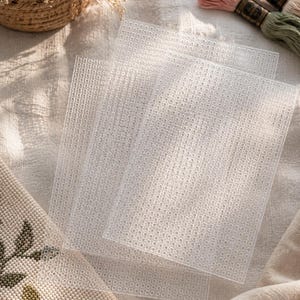 Op de afbeelding: Drie rechthoekige vellen doorzichtig plastic stramien met een uniform raster van kleine, ronde gaatjes. Deze halfdoorzichtige knutselvellen zijn licht overlappend gerangschikt en tonen het consistente geperforeerde patroon op elk stuk.