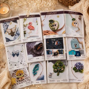 May include: A collection of Abris Art embroidery kits featuring various beaded designs including a bee, flamingo, apple, pear, bow, feather, fox, ice cream cone, owl, leaf, and hydrangea, each packaged in a clear plastic sleeve with product labels.