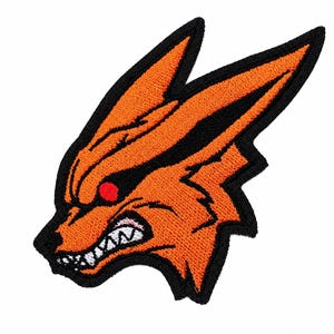 May include: An embroidered patch featuring the head of a stylised orange fox with pointed ears, a black outline, a single red eye, and an open mouth showing white teeth. The design is rendered in vibrant orange thread against a black border.