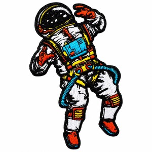 May include: An embroidered patch featuring an astronaut in a white suit with black, orange, yellow, and blue accents. The astronaut is depicted in a floating pose with a black helmet visor, a blue chest pack, and orange gloves and boots.