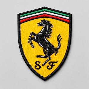 May include: A shield-shaped embroidered patch featuring a yellow background with a black prancing horse in the center. At the top, there are horizontal stripes of green, white, and red. The letters S and F are stitched in black at the bottom.