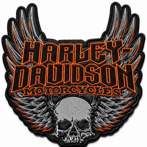 May include: An embroidered patch featuring the text HARLEY-DAVIDSON MOTORCYCLES in black with orange borders. The design includes large stylized wings in silver and black with orange accents, and a detailed grey skull at the bottom center.