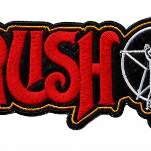 May include: An embroidered fabric patch featuring the word RUSH in bold red lettering with a black and yellow border. To the right of the text is a white star emblem containing a silhouette of a person standing with one arm raised upward.