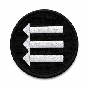 May include: A circular embroidered patch with a black background and a white graphic design. The design features a vertical line of three white arrowheads pointing left, each connected to a horizontal white bar extending to the right edge.