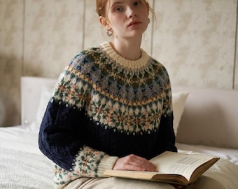 Può includere: Un maglione in maglia a maniche lunghe con girocollo e polsini a coste color crema. La parte superiore del petto e le spalle presentano un motivo multicolore nei toni del verde, blu e rosa, mentre la parte inferiore è di colore blu scuro.