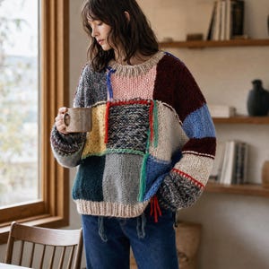 Könnte beinhalten: Ein langärmeliger Pullover mit einem Patchwork-Design aus verschiedenen Stricktexturen und Farben, darunter Rosa, Burgunderrot, Gelb, Blau, Grau und Creme. Das Kleidungsstück hat einen gerippten Rundhalsausschnitt, Bündchen und einen Saum.