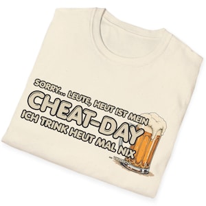 Może przedstawiać: Kremowa koszulka z napisem "SORRY... LEUTE, HEUT IST MEIN CHEAT-DAY ICH TRINK HEUT MAL NIX" i grafiką kufla piwa. Kufel jest wypełniony złotym piwem i białą pianą. Koszulka jest złożona.
