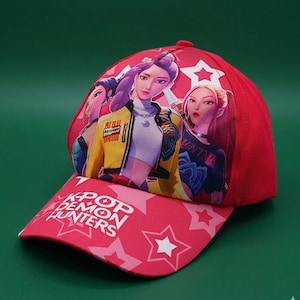 May include: Red baseball cap featuring a graphic of three anime-style women. The cap's brim displays the text "KPOP DEMON HUNTERS" with star patterns. The women are depicted in a vibrant style, with one wearing a yellow jacket.