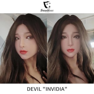 May include: A realistic silicone mask featuring a human-like face with long dark brown hair, defined eyebrows, brown eyes, and bright red lips. The mask displays smooth skin texture and is labeled with the text SecondFace and DEVIL INVIDIA.