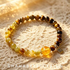 May include: A beaded bracelet featuring a gradient of polished tiger eye stones transitioning from dark brown to translucent golden yellow. The bracelet includes a single larger faceted yellow crystal bead and a small rectangular metal charm with Chinese text.