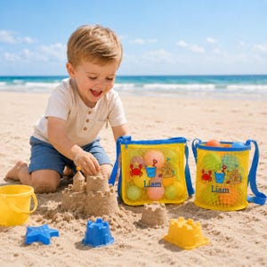 Może przedstawiać: Dziecko bawi się na piaszczystej plaży z zamkiem z piasku, ż&oacute;łtym wiadrem i niebiesko-ż&oacute;łtymi zabawkami plażowymi. Dwie ż&oacute;łte siatkowe torby z niebieskimi paskami są wypełnione kolorowymi piłkami i grafiką o tematyce plażowej. Na torbach wydrukowano imię "Liam".