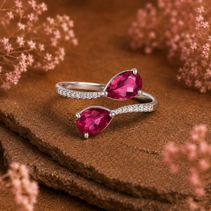 Puede incluir: Un anillo de plata tipo bypass con dos gemas de color rosa intenso en talla pera. La banda está dividida en dos extremos abiertos, cada uno acentuado con una hilera de pequeñas piedras claras de talla redonda engastadas a lo largo del metal.