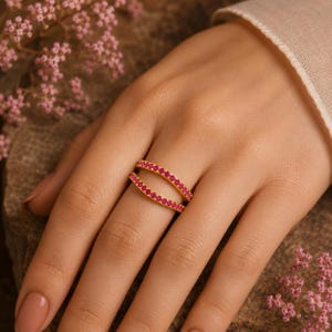 Pode incluir: Um anel de ouro com duas bandas paralelas, cada uma cravejada com uma fila cont&iacute;nua de pequenas pedras cor-de-rosa vibrantes. O design cria uma silhueta aberta e curva que envolve o dedo, exibindo um acabamento met&aacute;lico polido.