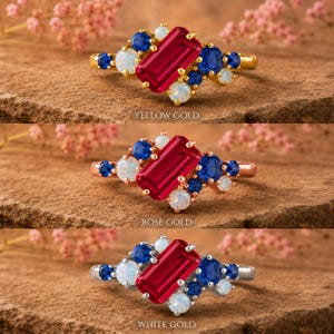 Op de afbeelding: Drie ringen met een centrale smaragdgeslepen rode edelsteen omringd door clusters van ronde blauwe saffieren en witte opalen. De bovenste ring is geelgoud, de middelste ros&eacute;goud en de onderste witgoud, elk voorzien van een bijbehorend label.