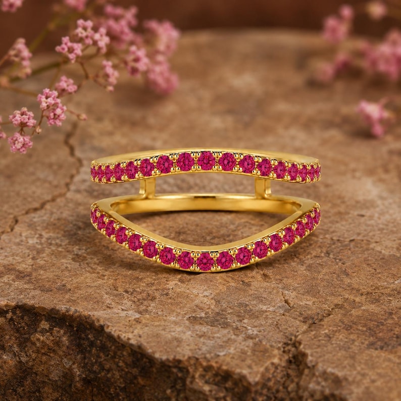 Pode incluir: Um anel de ouro com um design de banda dupla e uma silhueta aberta e curva. Ambas as bandas est&atilde;o incrustadas com pequenas pedras preciosas circulares de cor rosa vibrante dispostas numa fila cont&iacute;nua, criando um aspeto brilhante e colorido.