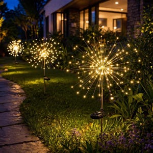 May include: Outdoor solar-powered decorative lights. The lights are shaped like starbursts with numerous small, warm white LED lights radiating from a central point. They are installed in a garden bed with green grass and foliage.