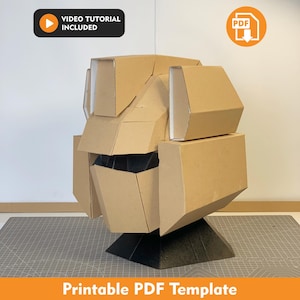 May include: A cardboard helmet model with geometric panels and a black base. The design features angular, layered sections in a tan color. Text in the image includes "VIDEO TUTORIAL INCLUDED", a PDF icon, and "Printable PDF Template" at the bottom.