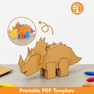 Puede incluir: Un dinosaurio triceratops en 3D hecho de cartón marrón. Un recuadro circular muestra una versión coloreada del mismo modelo de dinosaurio. Un icono de PDF se encuentra en la esquina superior derecha y el texto "Printable PDF Template" está en la parte inferior.