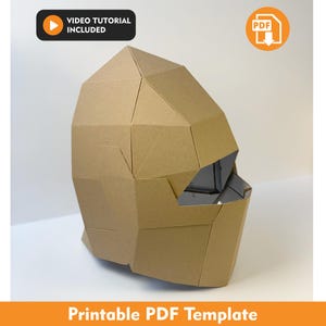 May include: A geometric helmet constructed from tan cardboard panels with a faceted, angular design. The structure features a wide eye opening and a solid chin guard. The image includes a video tutorial icon and a PDF download icon with text.