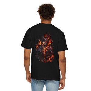 May include: Black t-shirt featuring a detailed graphic of a character engulfed in flames. The artwork depicts a person with fiery red and orange accents, set against a dark background. The design is centered on the back of the shirt.