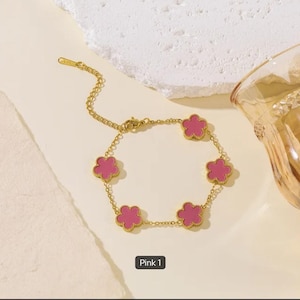 May include: A gold-tone chain bracelet featuring five evenly spaced flower-shaped charms with pink centers. The bracelet includes a delicate link chain with a lobster claw clasp and an adjustable extender chain. The text Pink 1 is visible below.