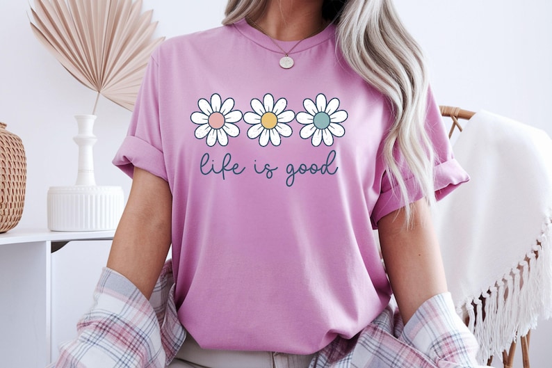Woman in a mauve great  t-shirt with colourful daisies and the motivational 'life is good' text.