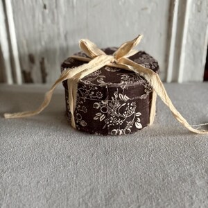 May include: A small round box with a floral pattern and a cream-colored ribbon tied around it.