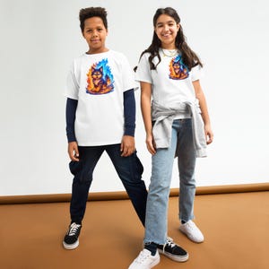 Könnte beinhalten: Zwei Kinder tragen weiße T-Shirts mit einer farbenfrohen Grafik einer Katze in Flammen. Die Katze ist in Blau-, Orange- und Gelbtönen dargestellt. Die Kinder tragen blaue Jeans und Turnschuhe.