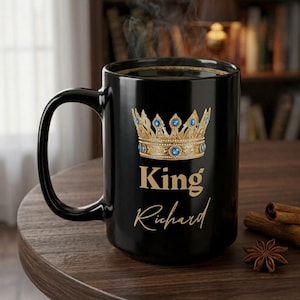 Op de afbeelding: Een zwarte keramische mok met een goudkleurige kroonafbeelding met blauwe ronde accenten. Onder de kroon staat het woord King in een vetgedrukt goudkleurig lettertype, gevolgd door de naam Richard in een goudkleurig cursief lettertype.