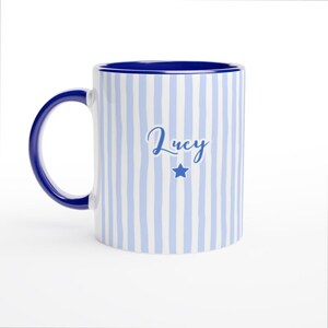 May include: A white ceramic mug with a black handle and the text "But First, Coffee" in a bold, black font. The mug is set against a blurred background, suggesting a cozy setting. The mug appears to be approximately 4 inches tall.