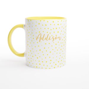 May include: White ceramic mug with a yellow interior and handle. The exterior is covered in yellow polka dots, and the name "Addison" is written in gold script.
