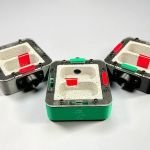 May include: Three square ant farms with clear tops, silver frames, and green or black bases. Each has a red and green accent, and a black tube. The ant farms are designed to house ants.